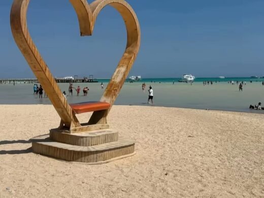 Large wooden heart sculpture on the sandy shore of Orange Bay island with turquoise water and boats