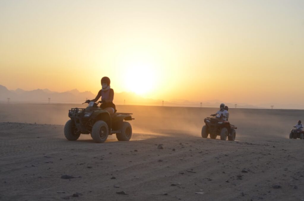 Touristen fahren mit Quads durch die Wüste bei Sonnenuntergang in Hurghada. Quad-Ausflug bei Sonnenuntergang